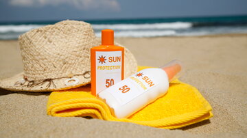 Sonnenschutzmittel und ein Sonnenhut liegen auf einem Handtuch an einem Sandstrand.