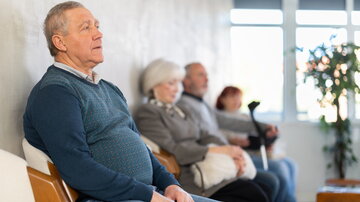 Gruppe älterer Menschen sitzt auf Stühlen in der Schlange, um den Arzt in der Lobby der medizinischen Einrichtung zu sehen