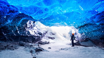 Ein Forscher steht in einer Gletscherhöhle, das Eis über ihm schimmert in Blautönen