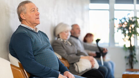 Gruppe älterer Menschen sitzt auf Stühlen in der Schlange, um den Arzt in der Lobby der medizinischen Einrichtung zu sehen