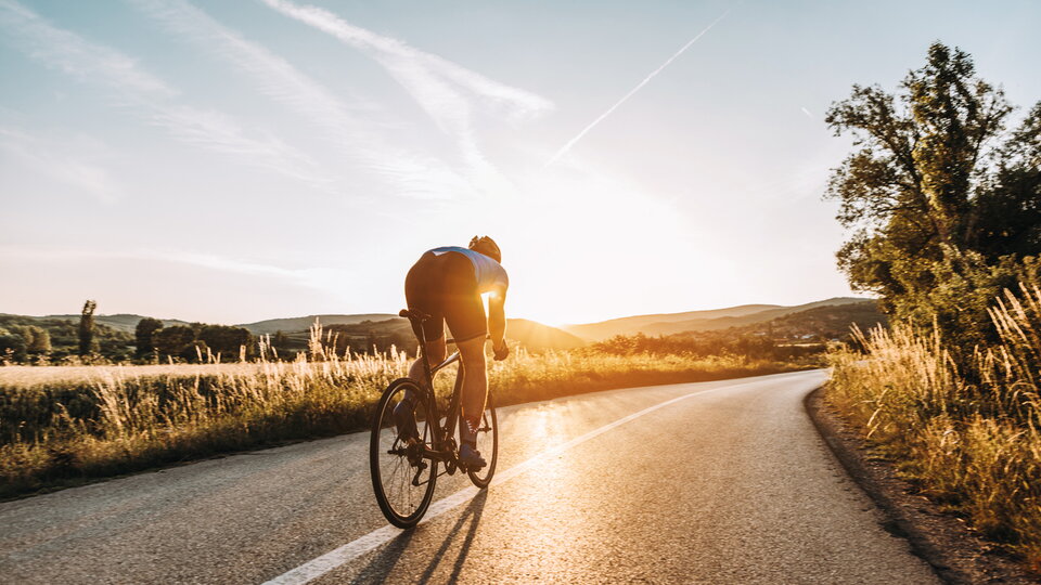 Ein Radfahrer fährt alleine auf einer sonnigen Straße.