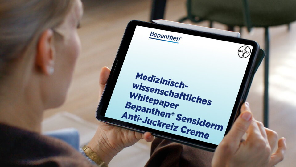 Eine Frau schaut sich auf einem Tablet das Whitepaper zu Bepanthen Sensiderm Anti-Juckreiz Creme an.