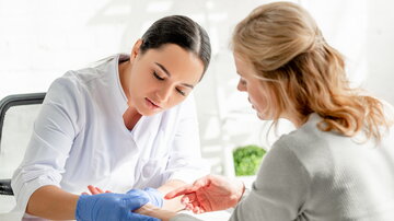 Dermatologin im weißen Arztkittel untersucht die Haut am Handgelenk einer Patientin