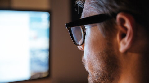 Ein Mann mit Brille schaut auf einen hell erleuchteten Monitor. Der Fokus des Bildes liegt auf dem Gesicht des Mannes.